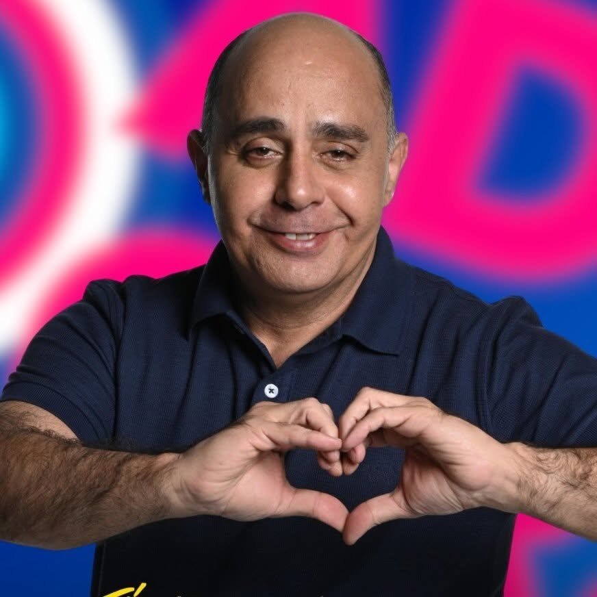 Foto de Adler Girão sorrindo, de camisa polo azul-marinho, fazendo um coração com as mãos.